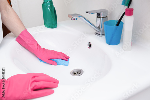 Fototapeta Naklejka Na Ścianę i Meble -  Home cleaning in the bathroom. A woman in pink gloves cleaning a white sink with a sponge and spray and detergent. Hygiene at home, house cleaning, keeping clean.