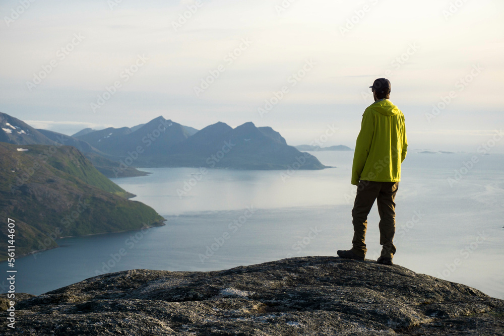 Young male hiker stands at the top of a mountain near Tromsø Norway overlooking fjords Young male hiker stands at the top of a mountain near Tromsø Norway overlooking fjords
