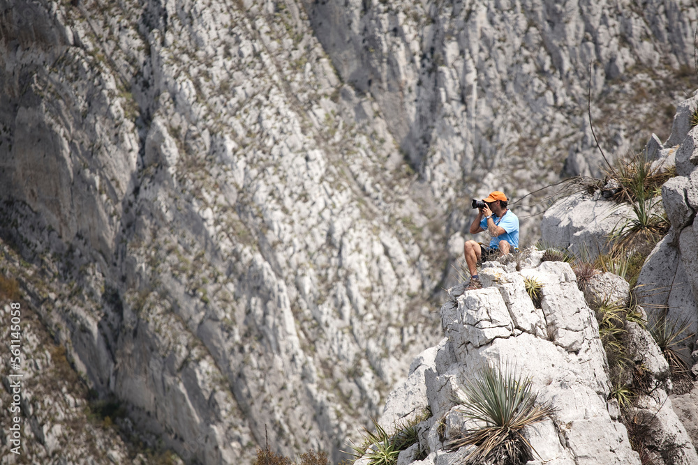A man using a photo camera sitting on a rock in La Huaseca, Nuevo Leon, Mexico. A man using a photo camera sitting on a rock in La Huaseca, Nuevo Leon, Mexico.