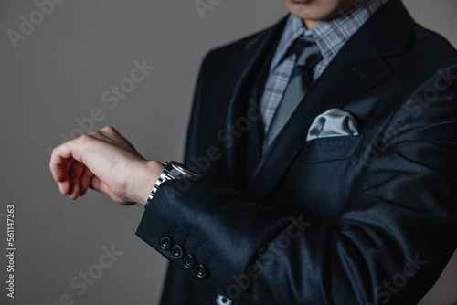 Smart young man in three-piece luxury black suit with a titanium watch on gray background.