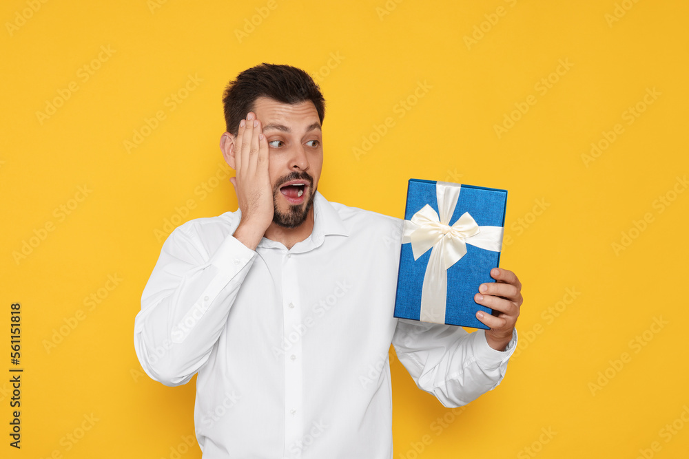 Surprised man with gift box on yellow background Surprised man with gift box on yellow background
