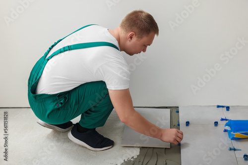 Worker installing ceramic tile on floor near wall