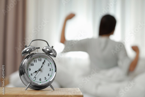 Woman stretching in bedroom, focus on alarm clock. Space for text