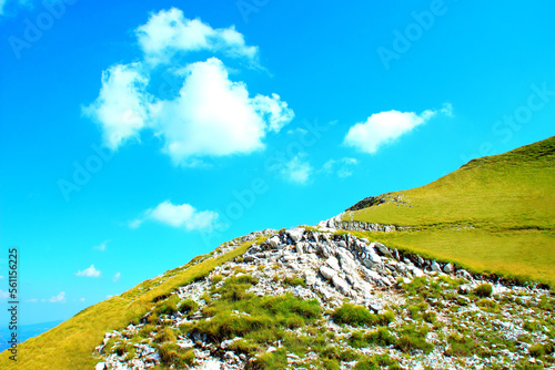 Heavenly view from Sassotetto at a slope of the Sibillini mountains with pure white rocks interspersed with green vegetation and surrounded by green grass under a perfect blue sky with puffy clouds photo