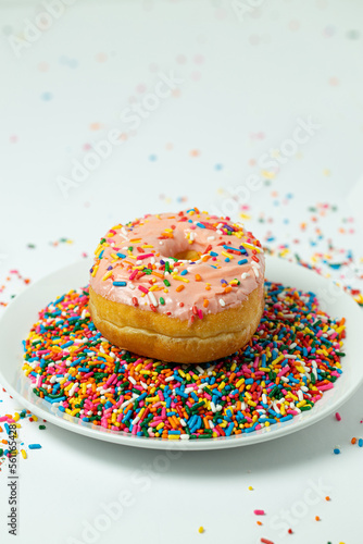 Pink donut with sprinkles on plate of sprinkles 