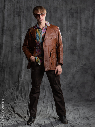 confident dude in a colorful shirt and brown leather jacket, a portrait in sunglasses in the studio on a gray background