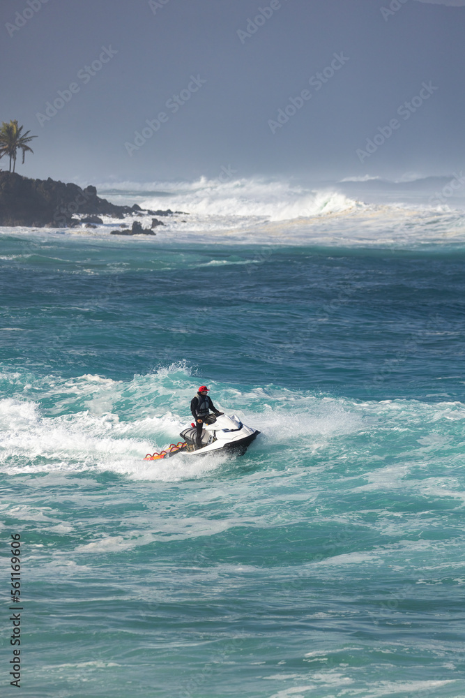 Rescue lifeguard riding a jet sky during big winter swell at North shore Oahu Hawaii, looking and helping surfers 