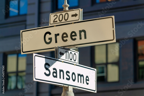 White and black road sign that says sansome and green with dense urban background in shade and sun midday © Aaron