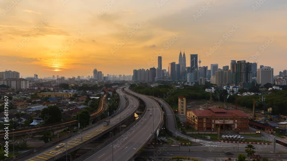 High angle aerial sunset view time lapse overlooking busy expressway and streets against a city skyline and an urban village at dusk in Kuala Lumpur, Malaysia. Zoom out motion timelapse. High angle aerial sunset view time lapse overlooking busy expressway and streets against a city skyline and an urban village at dusk in Kuala Lumpur, Malaysia. Zoom out motion timelapse.