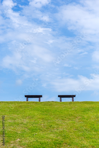 Public bench seat on green grass slope in Ang Kaew reservoir with cloudy blue sky background