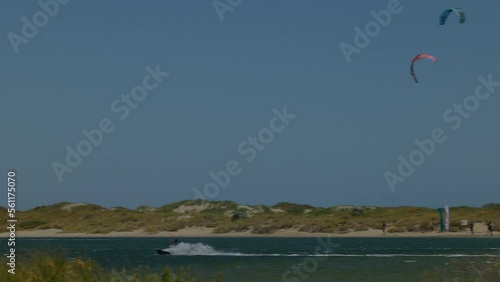Pan follow a kite surfer speeding across water and leaping into the air above Safety Bay - other surfers sail in background with sand dunes behind