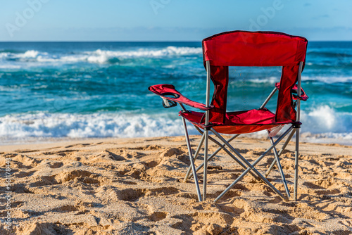 Stampa su tela An empty red beach chair facing the water on Sunset Beach, Hawaii