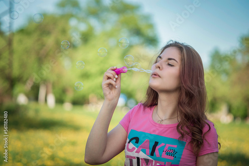 A young beautiful girl blows soap bubbles in nature.