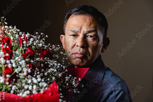 Middle-aged Asian man sending red roses and hazel to his loving wife. Concept photo of wedding anniversaries, entrance ceremonies and daily appreciation.