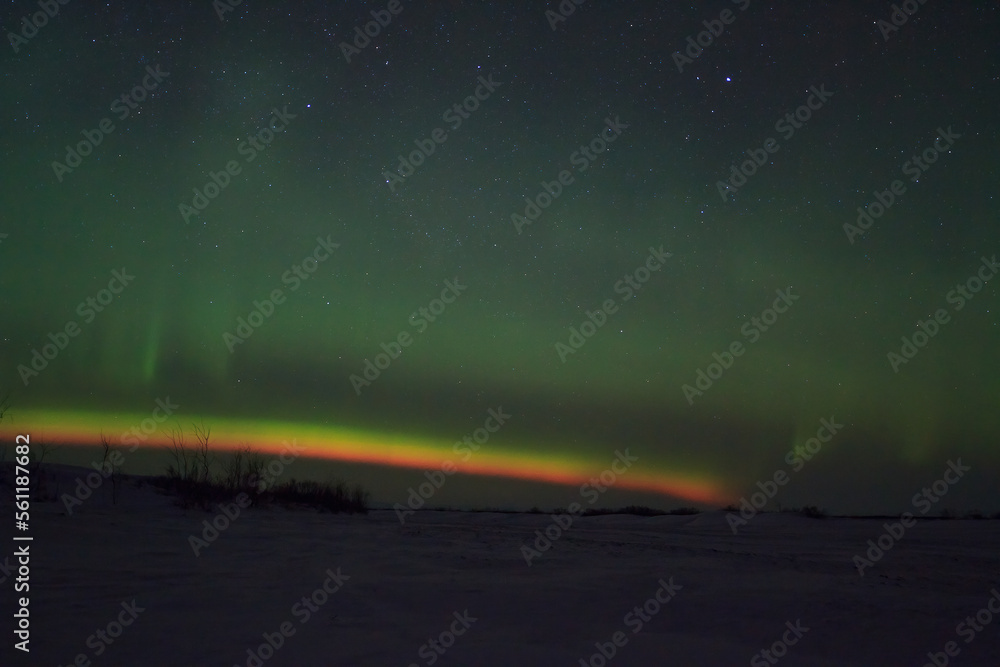 Night winter Arctic landscape. There are aurora borealis and stars in the sky above the horizon. A snow-covered river valley in the tundra. Multicolored northern lights. The polar region.