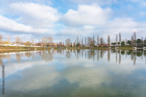 Panoramic view of a large lake in a public park where the cloudy sky and the trees of the shore are reflected, Tres Cantos, Madrid.