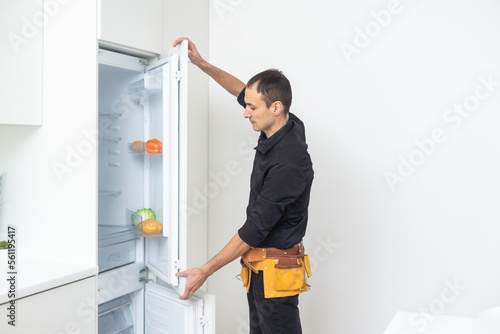 Young Male Repairman Fixing Refrigerator In Kitchen