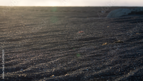 In this picture you can see a black sand beach. The close-up shows fine, small rocks beautifully lit by a sunset. The main colors here are yellow and grey. photo