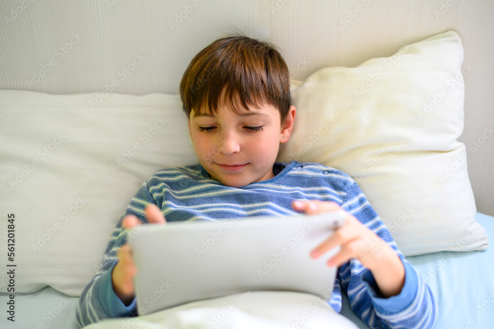 Fototapeta premium Smiling boy lying on his bed looking at a tablet