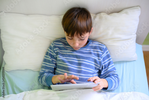 Boy lying on the bed looking at a tablet, top view