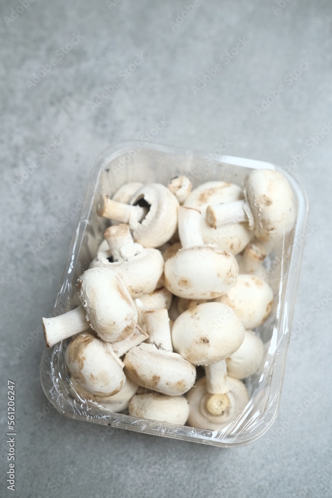 Champignon mushrooms in the plastic box at the grey background Champignon mushrooms in the plastic box at the grey background