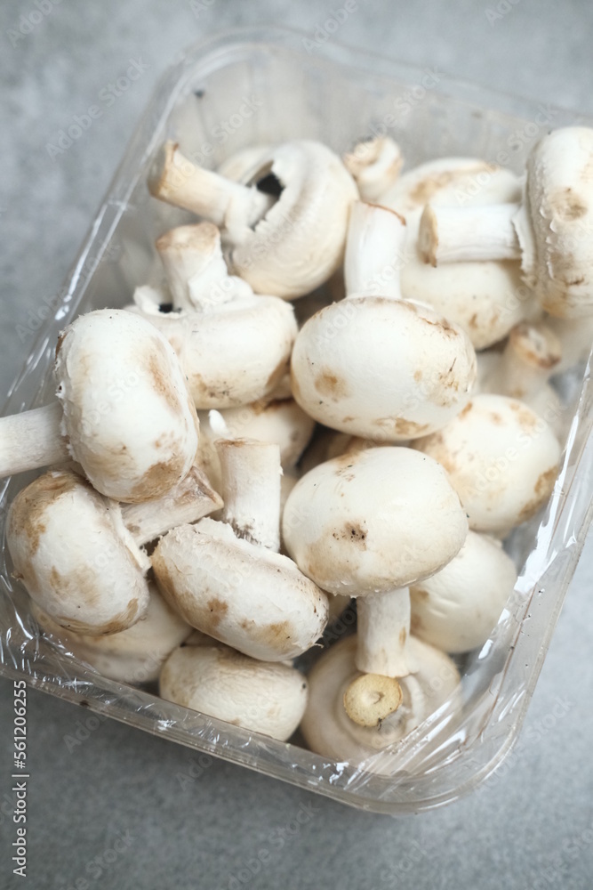 Champignon mushrooms in the plastic box at the grey background	