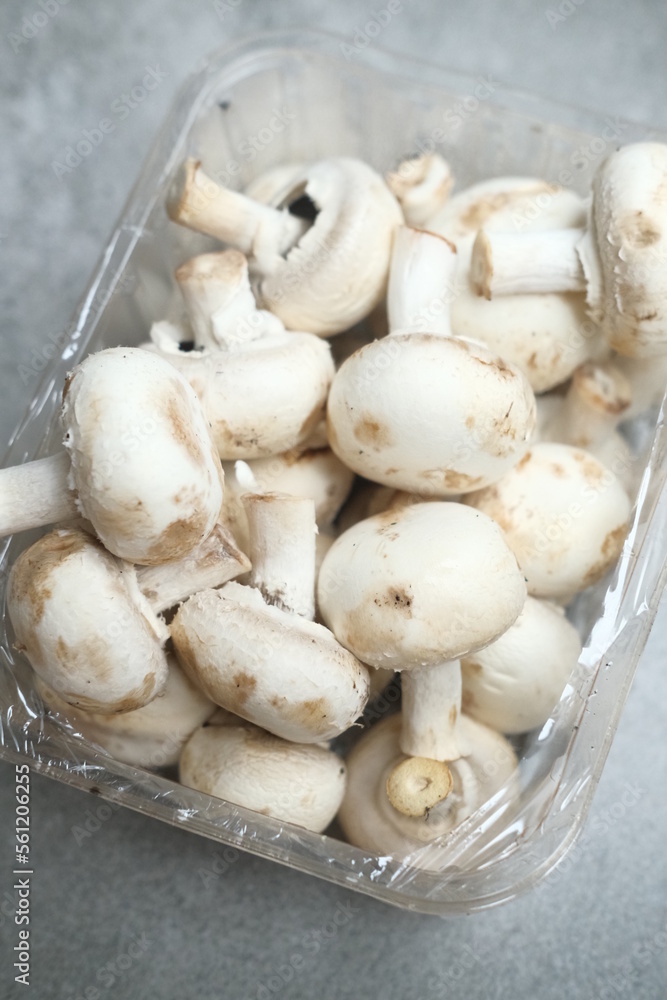 Champignon mushrooms in the plastic box at the grey background Champignon mushrooms in the plastic box at the grey background