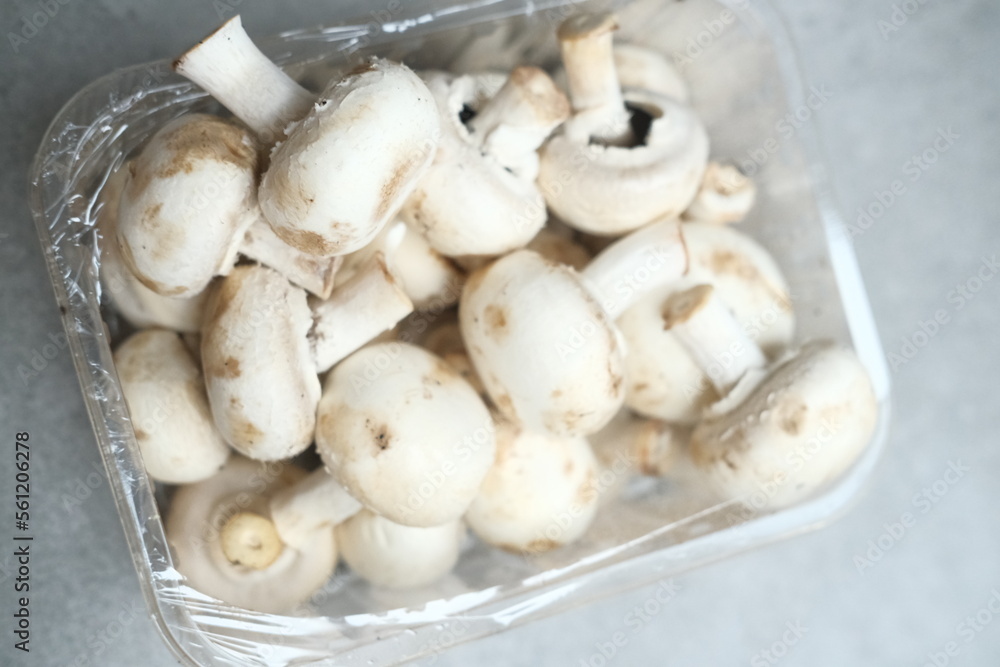 Champignon mushrooms in the plastic box at the grey background Champignon mushrooms in the plastic box at the grey background