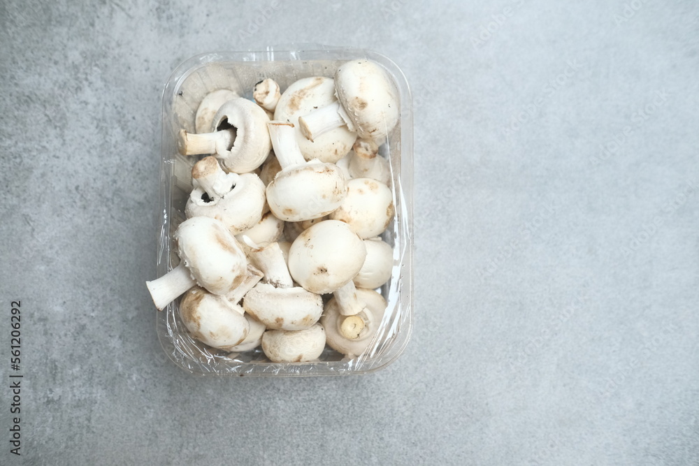 Champignon mushrooms in the plastic box at the grey background Champignon mushrooms in the plastic box at the grey background