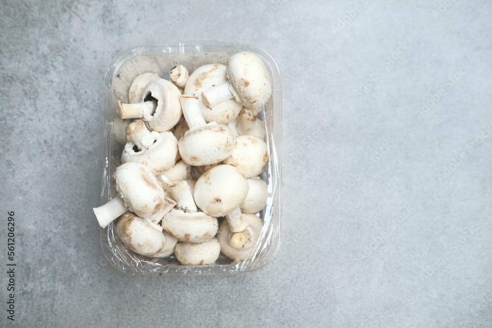 Champignon mushrooms in the plastic box at the grey background Champignon mushrooms in the plastic box at the grey background