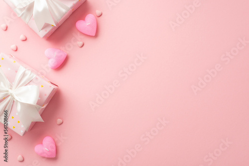 Saint Valentine's Day concept. Top view photo of stylish gift boxes with white ribbon bows heart shaped candles and sprinkles on isolated pastel pink background with blank space © ActionGP