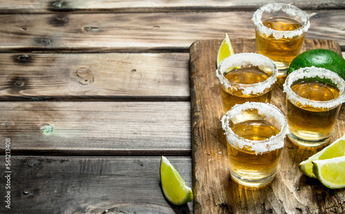 Tequila in a shot glass on a cutting Board with slices of lime.