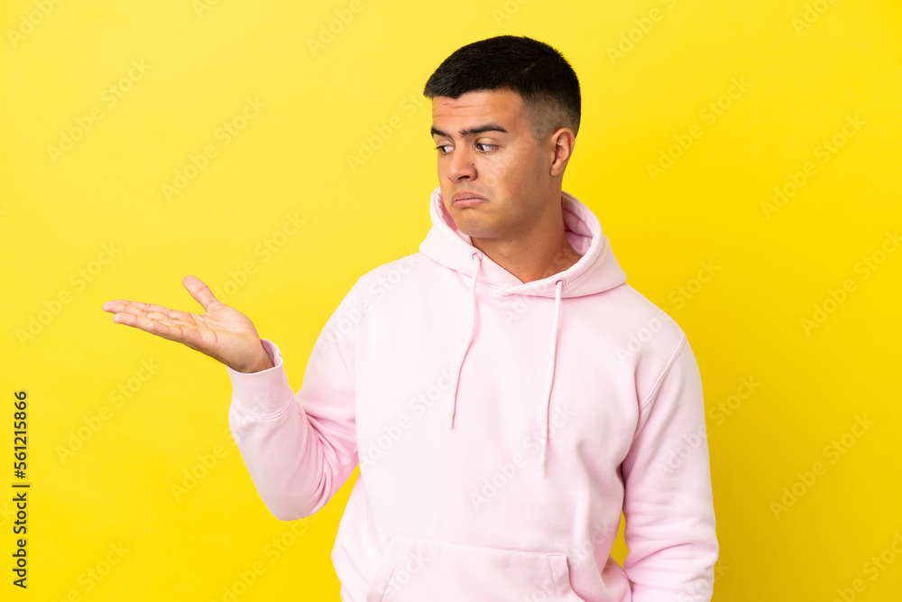 Young handsome man over isolated yellow background holding copyspace with doubts