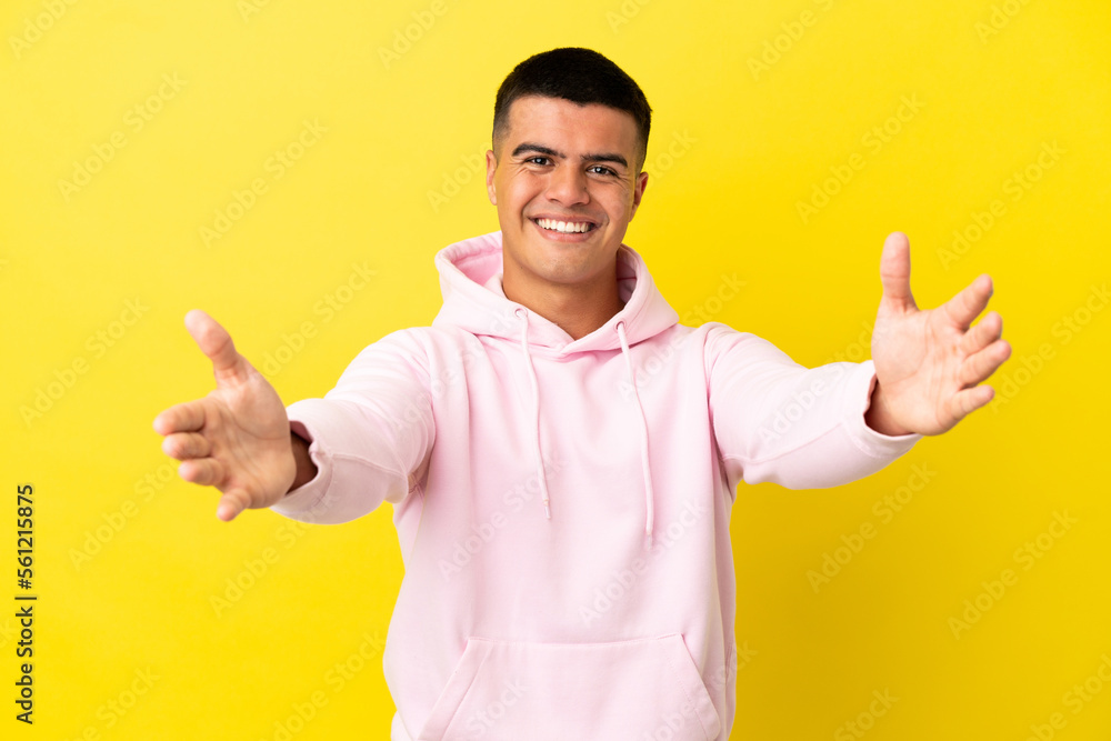 Young handsome man over isolated yellow background presenting and inviting to come with hand Young handsome man over isolated yellow background presenting and inviting to come with hand