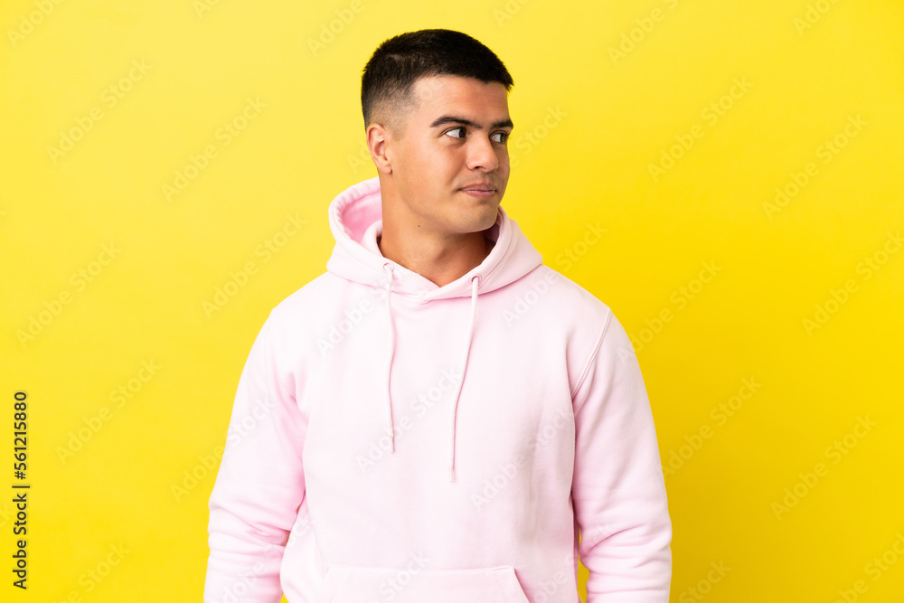 Young handsome man over isolated yellow background making doubts gesture looking side Young handsome man over isolated yellow background making doubts gesture looking side