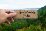 Hand holding wooden banner with Good Morning Friday text. With beautiful nature background. Morning wishes concept.