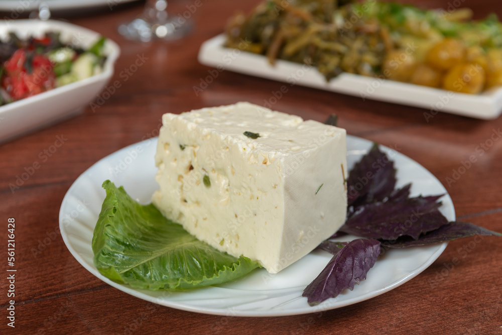 Big white piece of asian Korean tofu soy cheese on wooden board with greens