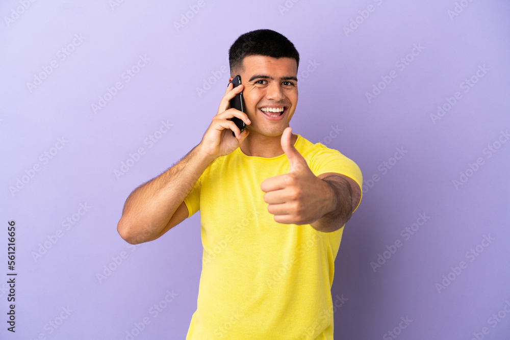 Young handsome man using mobile phone over isolated purple background with thumbs up because something good has happened Young handsome man using mobile phone over isolated purple background with thumbs up because something good has happened