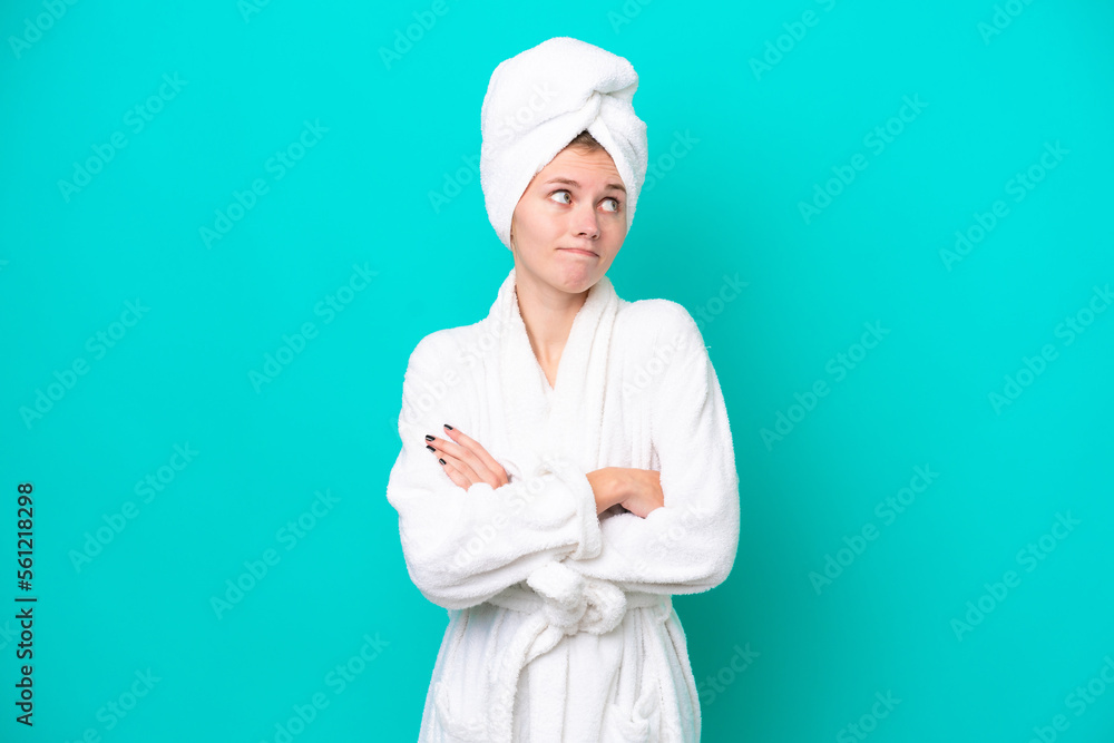 Young woman in a bathrobe isolated on blue background making doubts gesture while lifting the shoulders Young woman in a bathrobe isolated on blue background making doubts gesture while lifting the shoulders