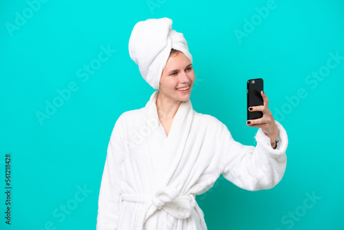 Young woman in a bathrobe isolated on blue background making a selfie