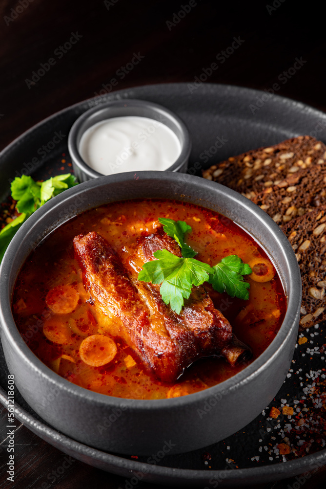 Solyanka soup with meat, sausage, vegetables, olives and lemon in bowl on wooden table background Solyanka soup with meat, sausage, vegetables, olives and lemon in bowl on wooden table background