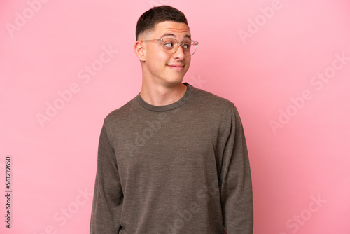 Young Brazilian man isolated on pink background making doubts gesture looking side © luismolinero