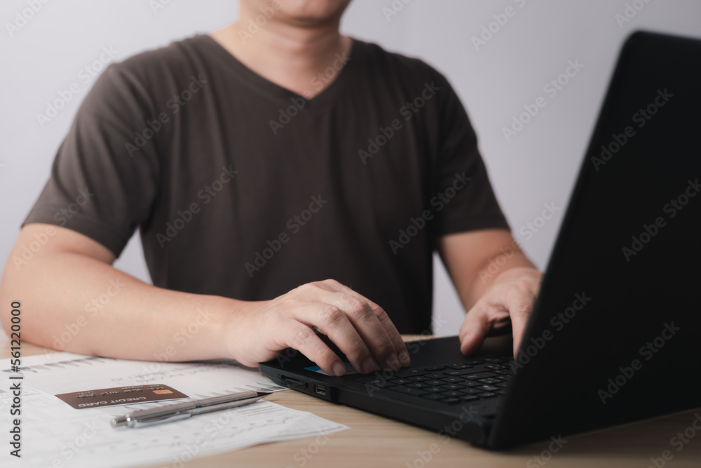 Men use laptop computers and credit card for business commerce, which is payment online, sits on the chair in the living room at home on a laptop. The concept of finance and online shopping. Men use laptop computers and credit card for business commerce, which is payment online, sits on the chair in the living room at home on a laptop. The concept of finance and online shopping.