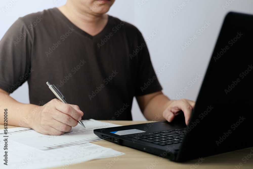 Man using laptop computer and taking notes in planning. which is payment online, sits on the chair in the living room at home on a laptop. The concept of finance and online shopping. Man using laptop computer and taking notes in planning. which is payment online, sits on the chair in the living room at home on a laptop. The concept of finance and online shopping.