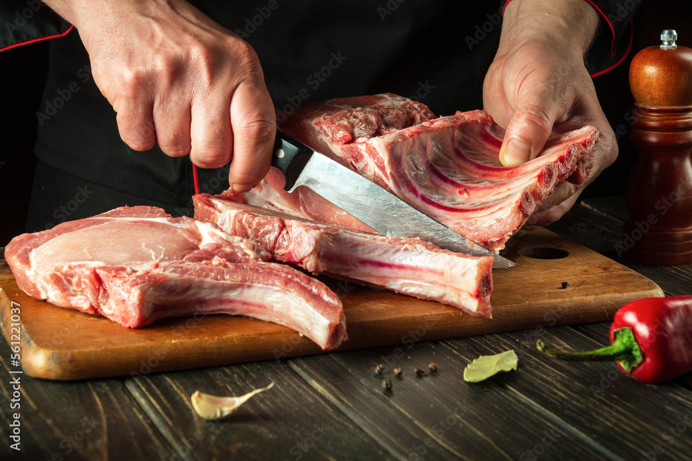 Chef cutting raw beef ribs with a sharp knife on wooden board. Process of cooking grilled bbq ribs. Asian cuisine.