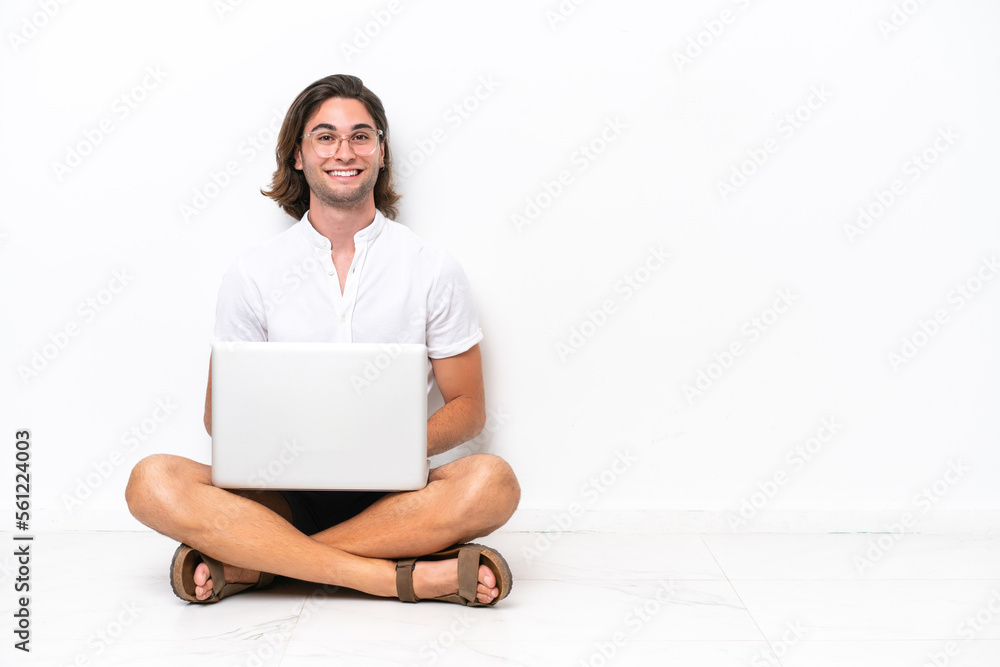 Young handsome man with a laptop sitting on the floor isolated on white background laughing Young handsome man with a laptop sitting on the floor isolated on white background laughing
