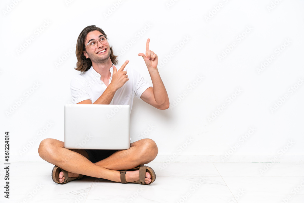 Young handsome man with a laptop sitting on the floor isolated on white background pointing with the index finger a great idea Young handsome man with a laptop sitting on the floor isolated on white background pointing with the index finger a great idea