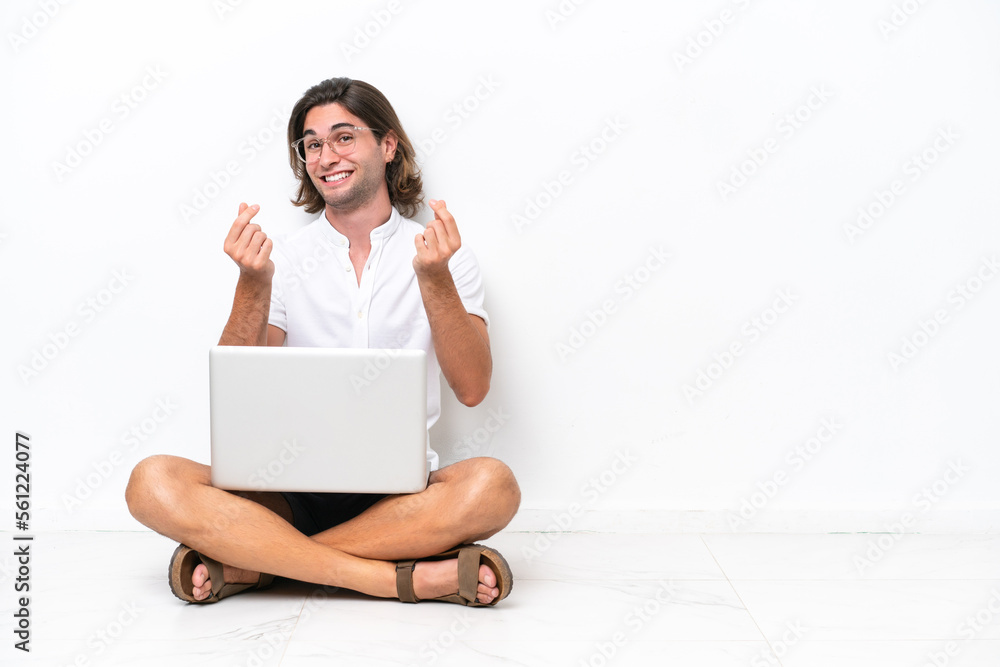 Young handsome man with a laptop sitting on the floor isolated on white background making money gesture Young handsome man with a laptop sitting on the floor isolated on white background making money gesture