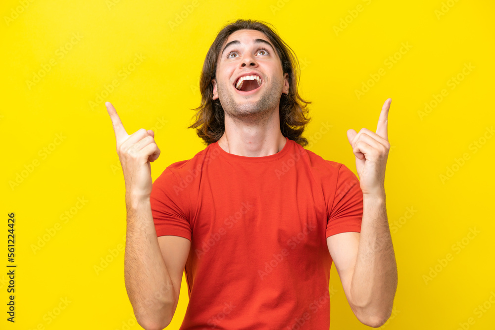 Caucasian handsome man isolated on yellow background surprised and pointing up Caucasian handsome man isolated on yellow background surprised and pointing up