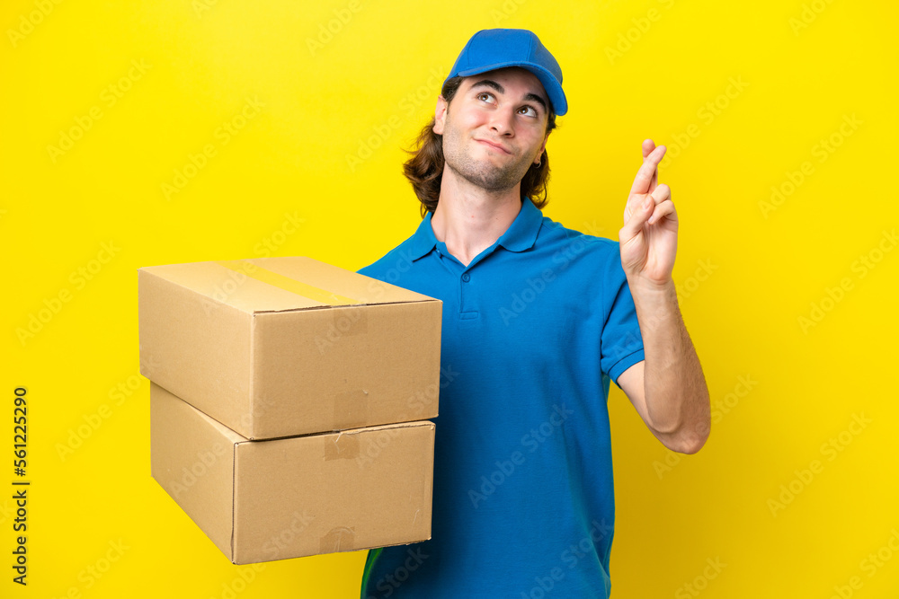 Delivery handsome man isolated on yellow background with fingers crossing and wishing the best Delivery handsome man isolated on yellow background with fingers crossing and wishing the best
